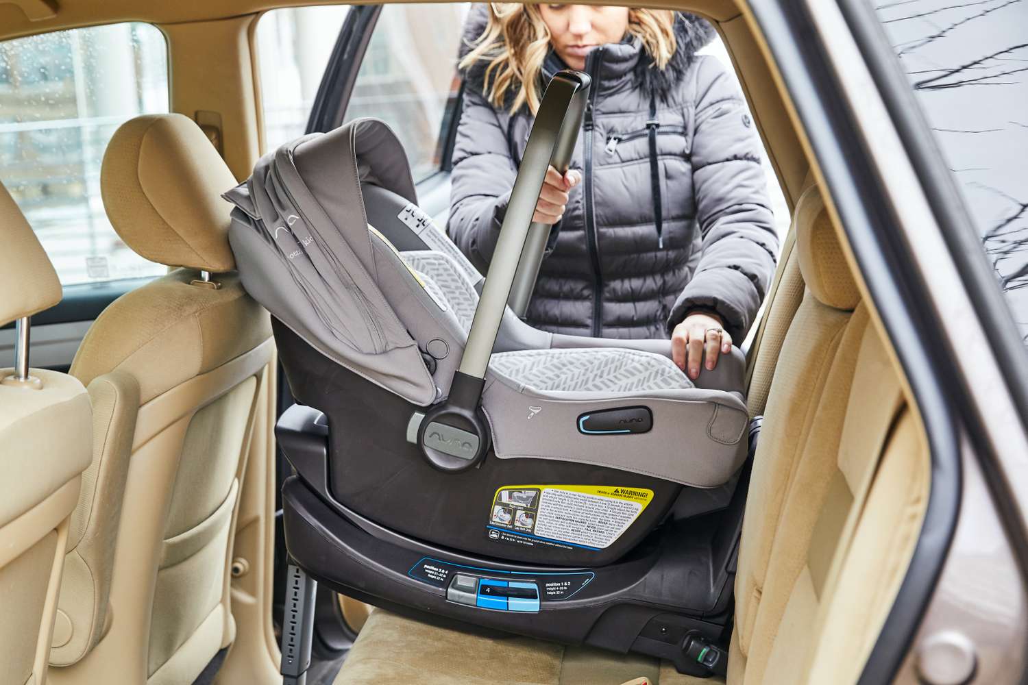 A woman carrying an infant car seat by the handle into the back seat of a car
