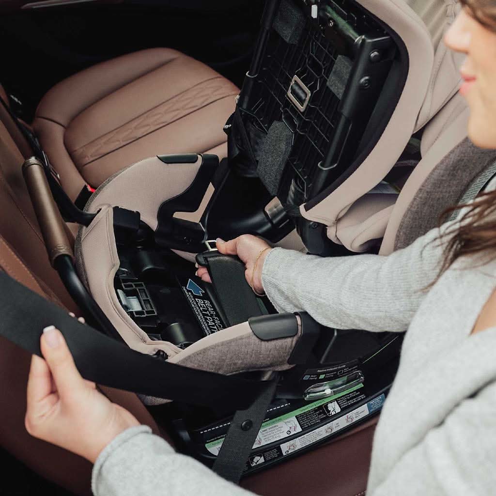 A Child Passenger Safety Technician threading a vehicle seat belt through the rear-facing belt path of a car seat